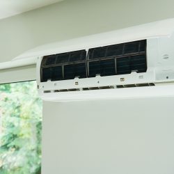 White air conditioner unit is mounted on wall, ready for maintenance. Climate system with opened front cover revealing internal components. Repairing HVAC in apartment