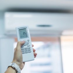 hand using remote controller for adjust Air conditioner inside the room of office or house