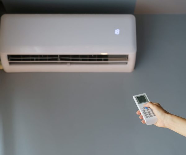 Owner uses remote control to turn on air conditioner hanging on grey wall. Modern technology allows people to make property more innovated. Landlady wants to warm up cold apartment using conditioner