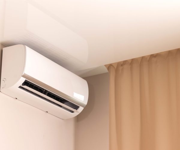 White air conditioner under stretch ceiling in modern room with beige curtains